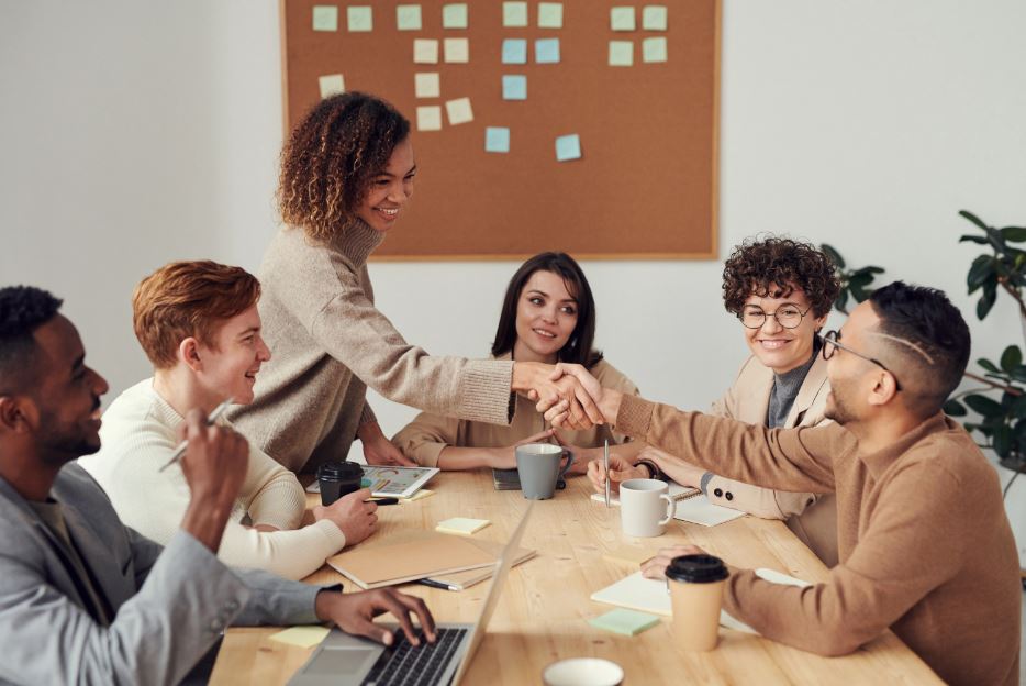 People sitting around a board table. Two people shake hands and agree to a digital marketing deal.